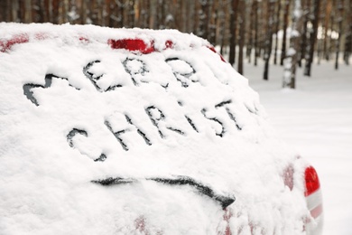 Phrase "Merry Christmas" written on snow covered car in winter forest. Space for text