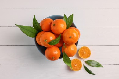 Photo of Bowl with fresh ripe juicy tangerines and green leaves on white wooden table, flat lay