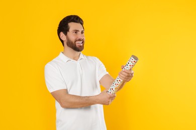Photo of Happy man with party popper on yellow background. Space for text