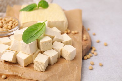 Photo of Delicious tofu cheese, basil and soybeans on light gray table, closeup