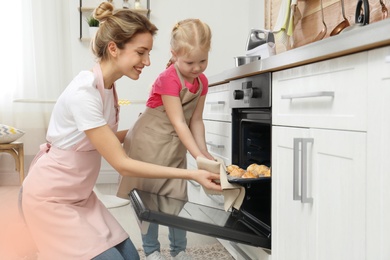 Mother and her daughter taking out cookies from oven in kitchen