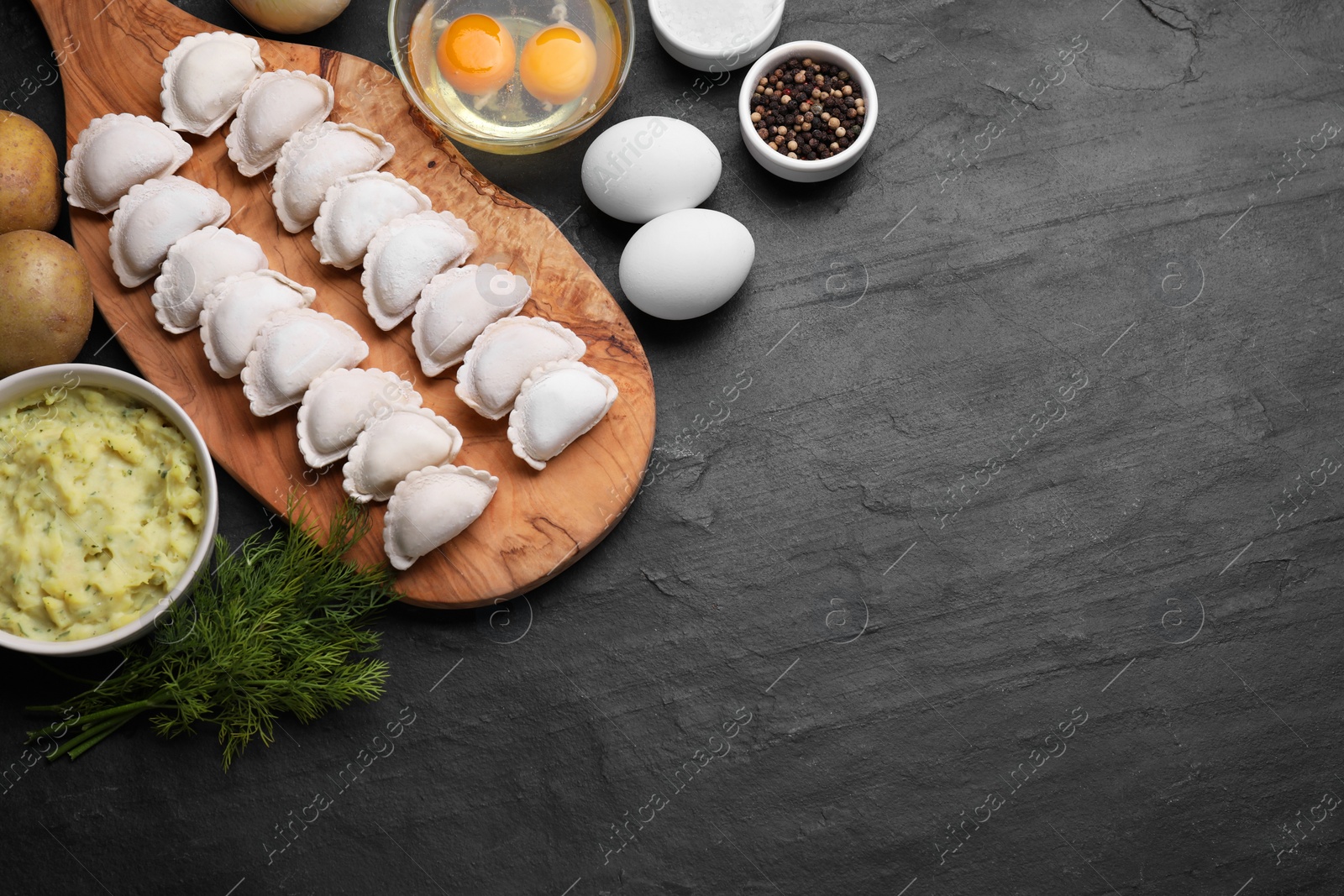 Photo of Raw dumplings (varenyky) and ingredients on black table, flat lay. Space for text