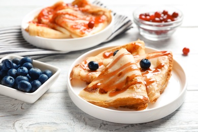 Thin pancakes served with syrup and berries on plates