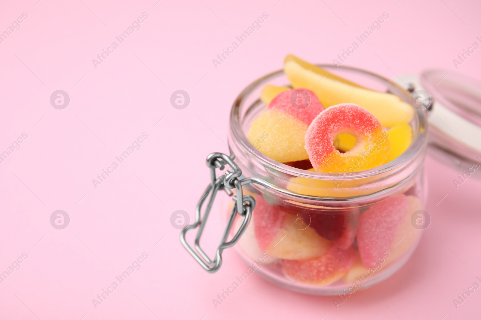 Photo of Tasty colorful jelly candies in glass jar on pink background, closeup. Space for text