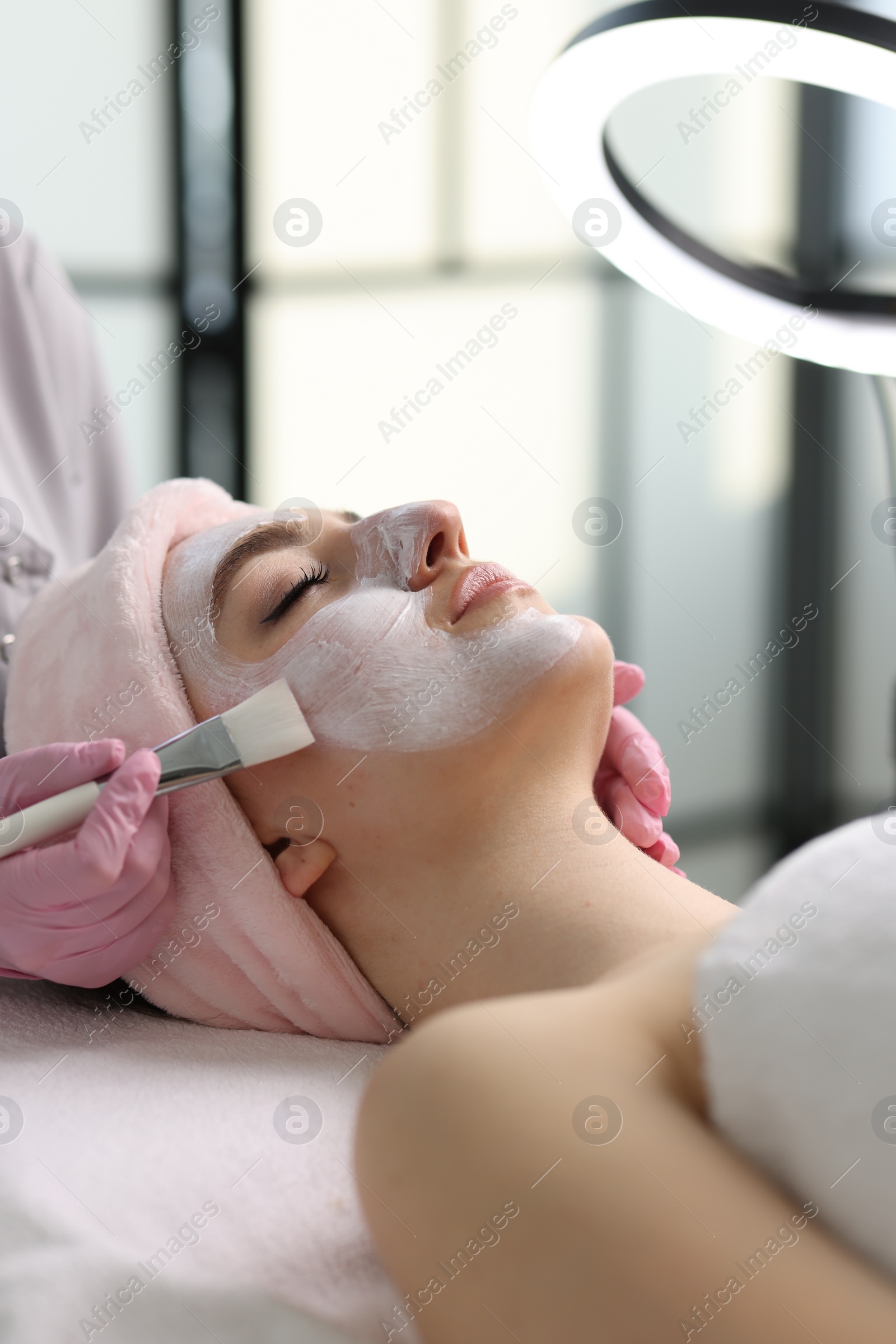 Photo of Cosmetologist applying mask on woman's face in clinic, closeup