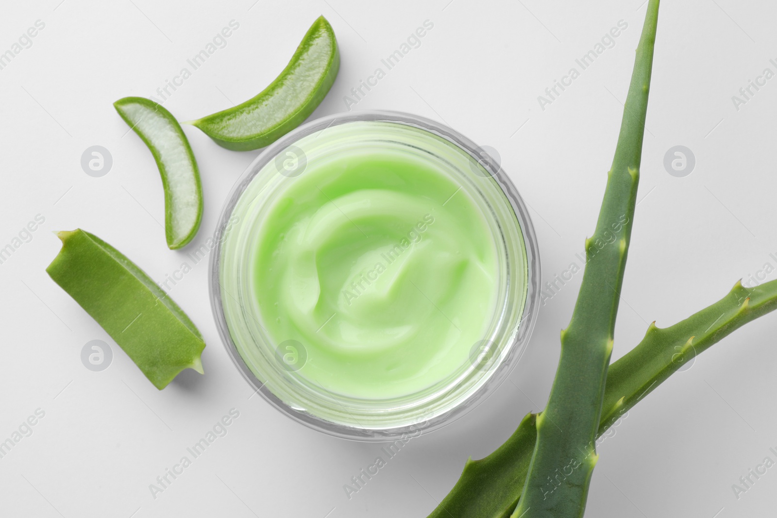 Photo of Jar of cosmetic cream and cut aloe leaves on white background, flat lay