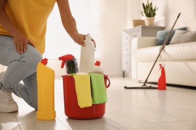 Photo of Woman holding bucket with cleaning supplies in living room, closeup
