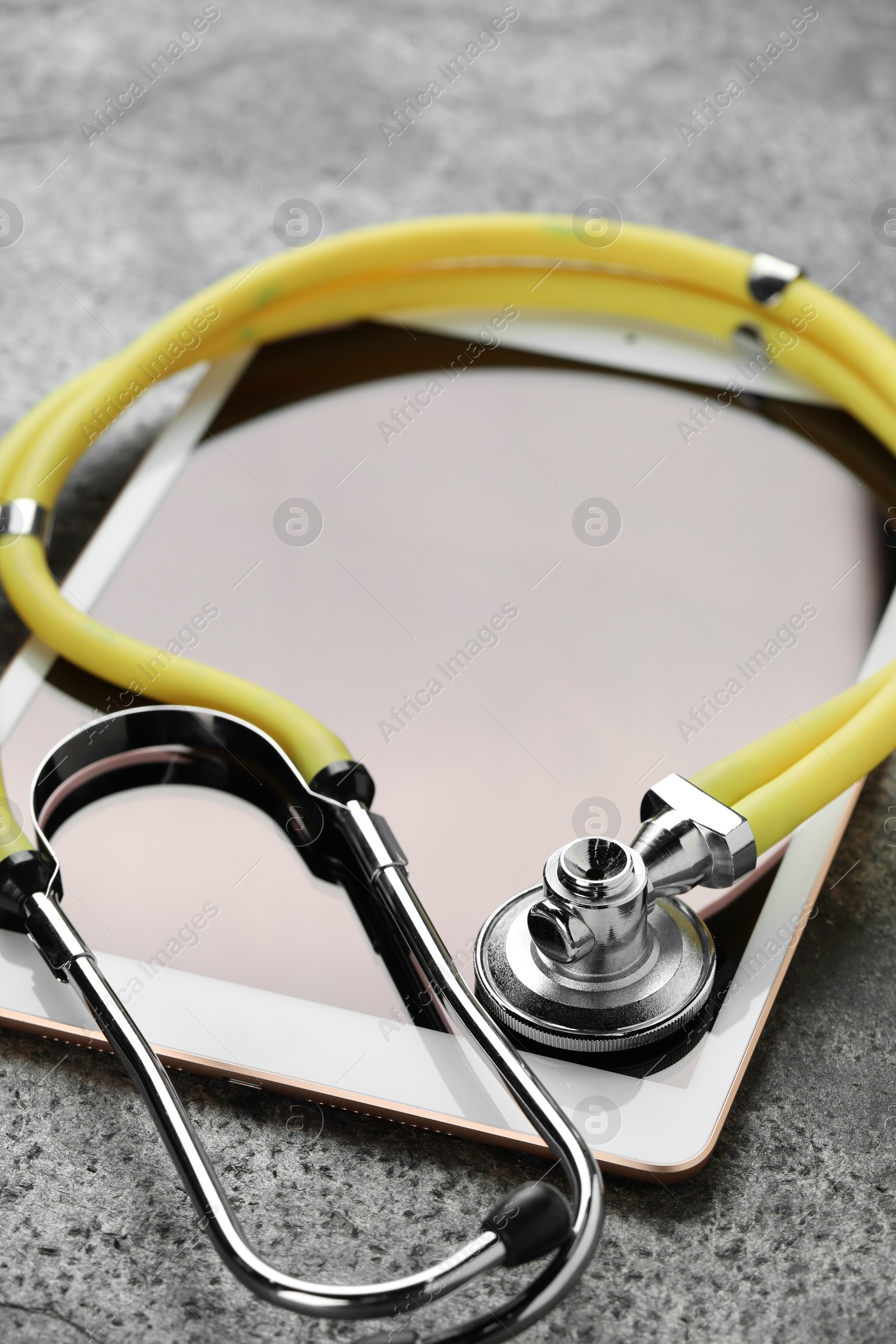 Photo of Modern tablet and stethoscope on grey table, closeup