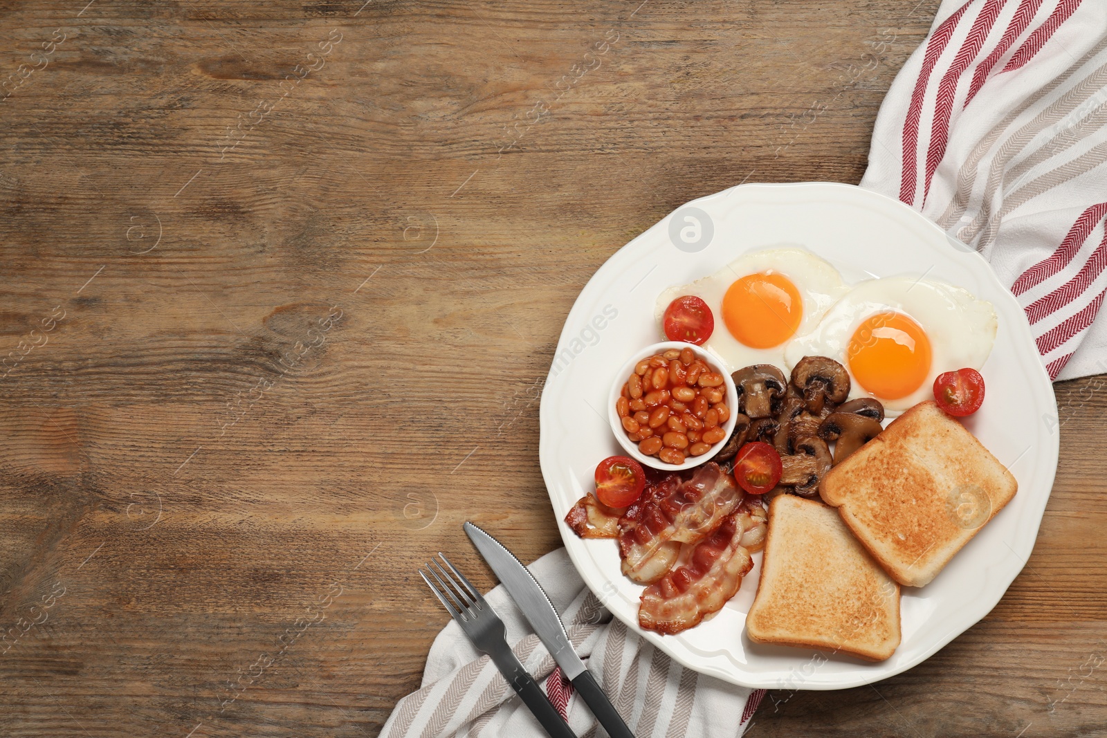 Photo of Plate of fried eggs, mushrooms, beans, bacon, tomatoes and toast on wooden table, flat lay with space for text. Traditional English breakfast