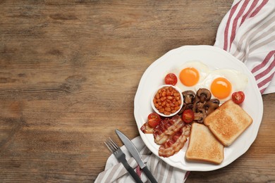 Photo of Plate of fried eggs, mushrooms, beans, bacon, tomatoes and toast on wooden table, flat lay with space for text. Traditional English breakfast