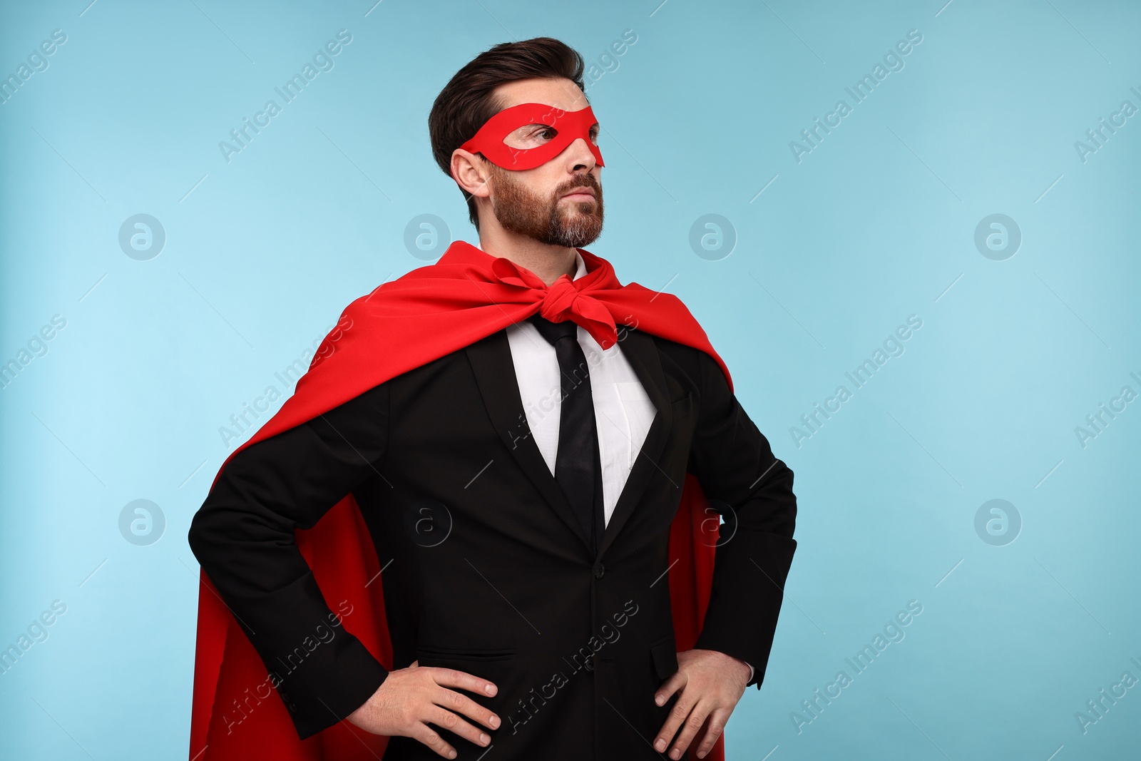 Photo of Businessman wearing red superhero cape and mask on light blue background. Space for text