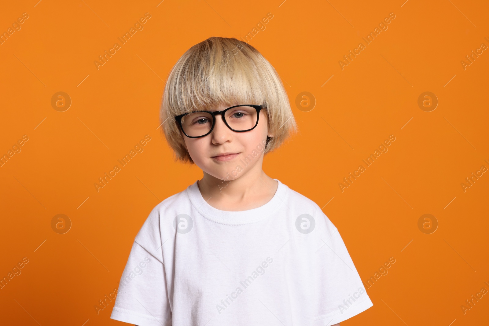 Photo of Cute little boy wearing glasses on orange background