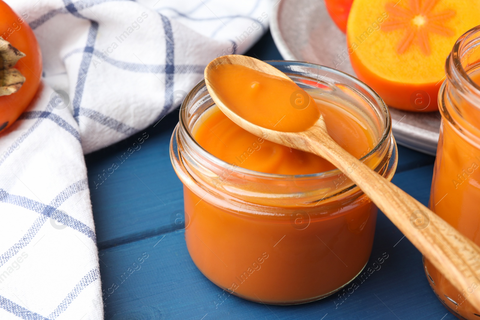 Photo of Delicious persimmon jam in glass jar served on blue wooden table, closeup