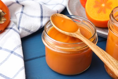 Photo of Delicious persimmon jam in glass jar served on blue wooden table, closeup