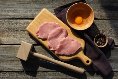 Photo of Cooking schnitzel. Raw pork slices, egg, peppercorns and meat tenderizer on wooden table, flat lay