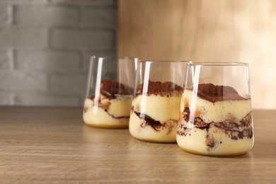 Delicious tiramisu in glasses on wooden table. Space for text