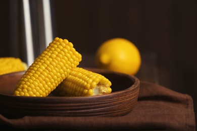 Photo of Plate with ripe corn cobs on table against dark background