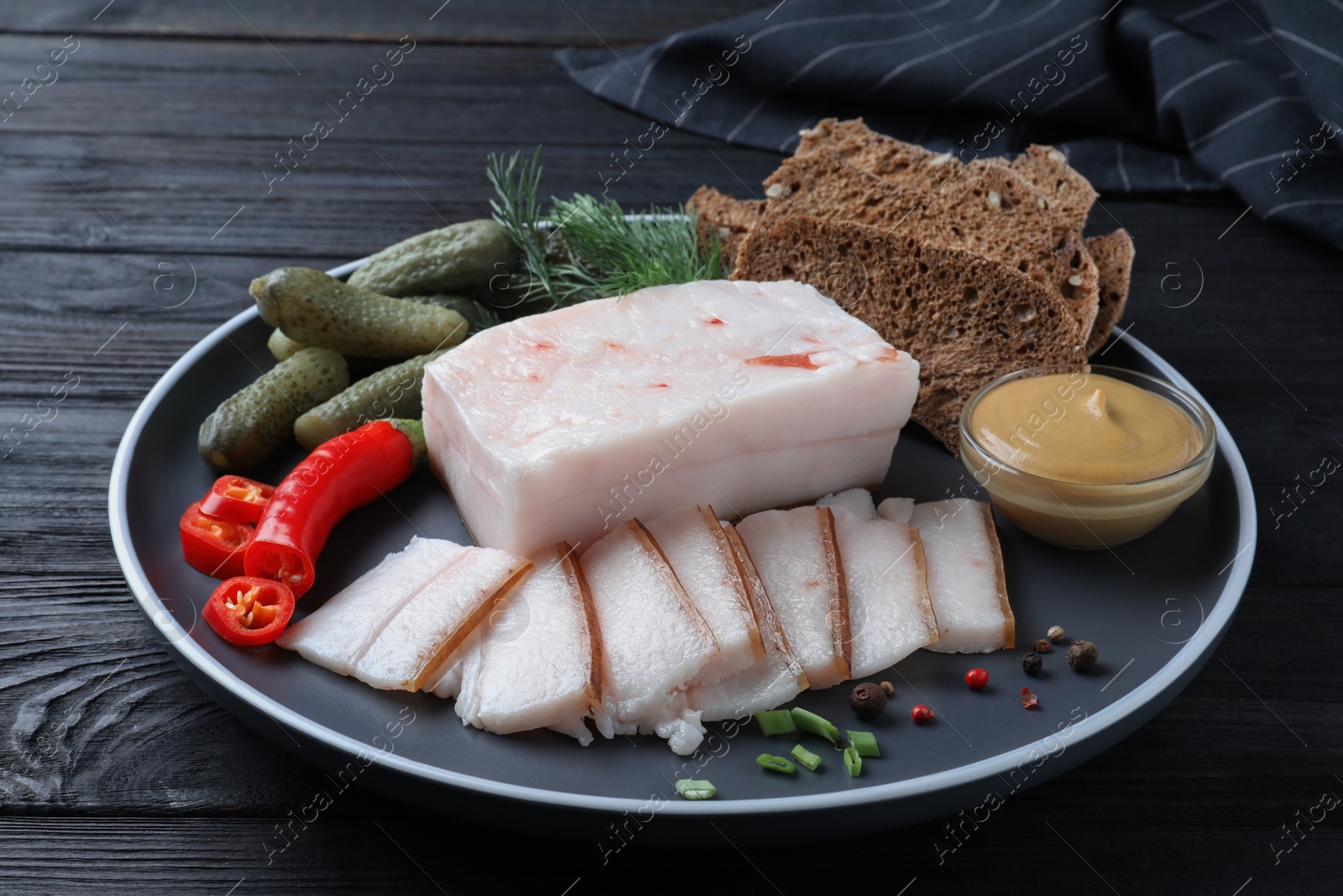 Photo of Pork fatback with spices, rye bread and pickled cucumbers on black wooden table