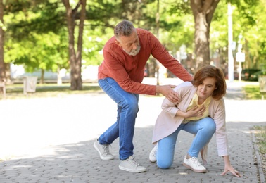 Photo of Man helping mature woman suffering from heart attack in park