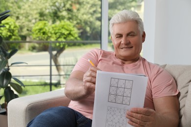 Senior man solving sudoku puzzle on sofa at home