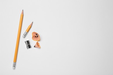 Photo of Graphite pencils, sharpener and shavings on white background, flat lay. Space for text