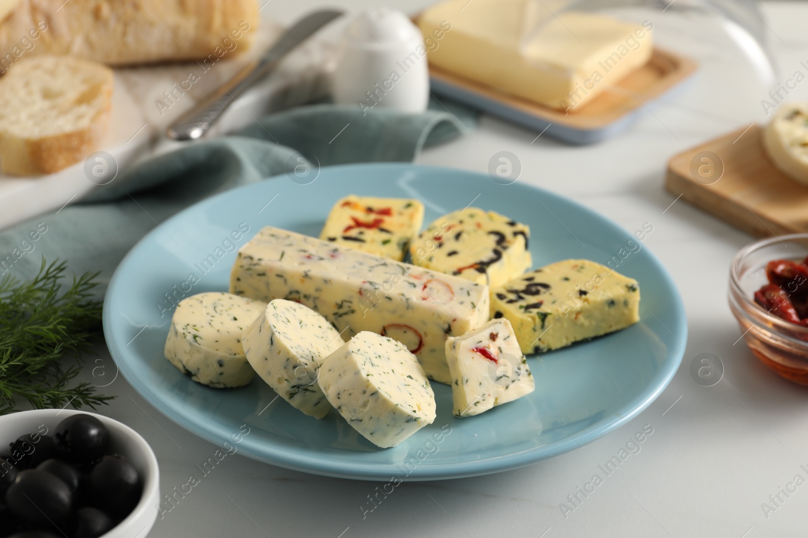 Photo of Different types of tasty butter, dill, olives and bread on white table