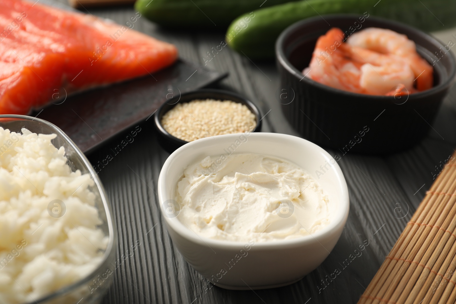 Photo of Cream cheese in bowl and other ingredients for sushi on black wooden table, closeup