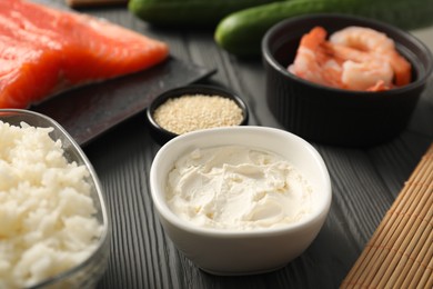 Photo of Cream cheese in bowl and other ingredients for sushi on black wooden table, closeup