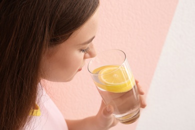 Young woman drinking lemon water on color background