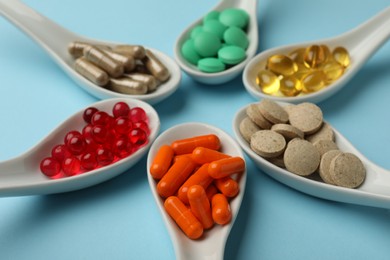 Spoons with different dietary supplements on light blue background, closeup