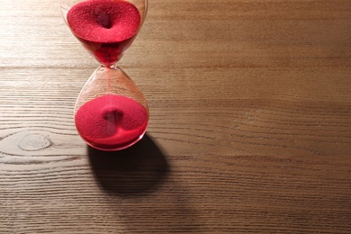 Hourglass with flowing red sand on wooden background. Time management