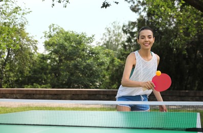 Photo of Young woman playing ping pong outdoors on summer day
