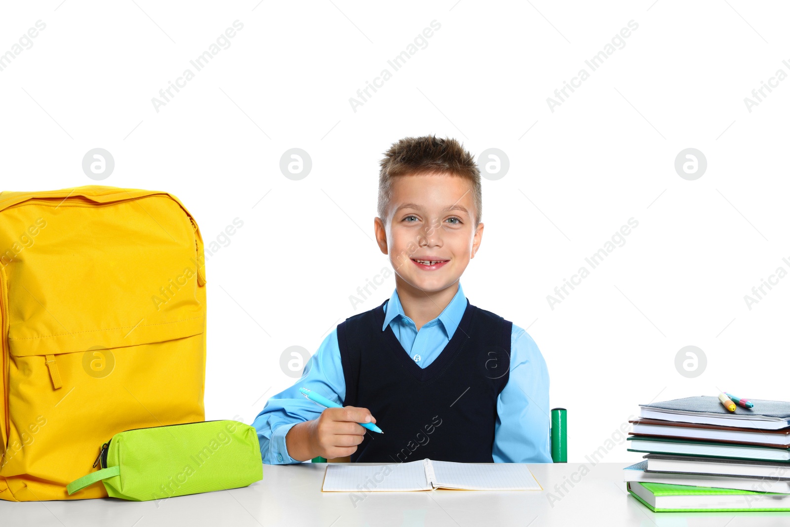 Photo of Little boy in uniform doing assignment at desk against white background. School stationery