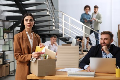 Young dismissed woman packing stuff into box at office