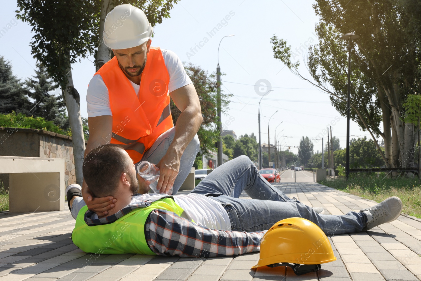 Photo of Worker with bottle of water helping colleague on city street. Suffering from heat stroke