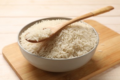 Photo of Raw basmati rice and spoon in bowl on white wooden table