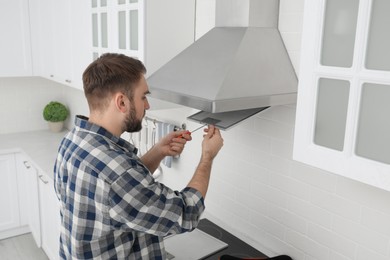 Man repairing modern cooker hood in kitchen