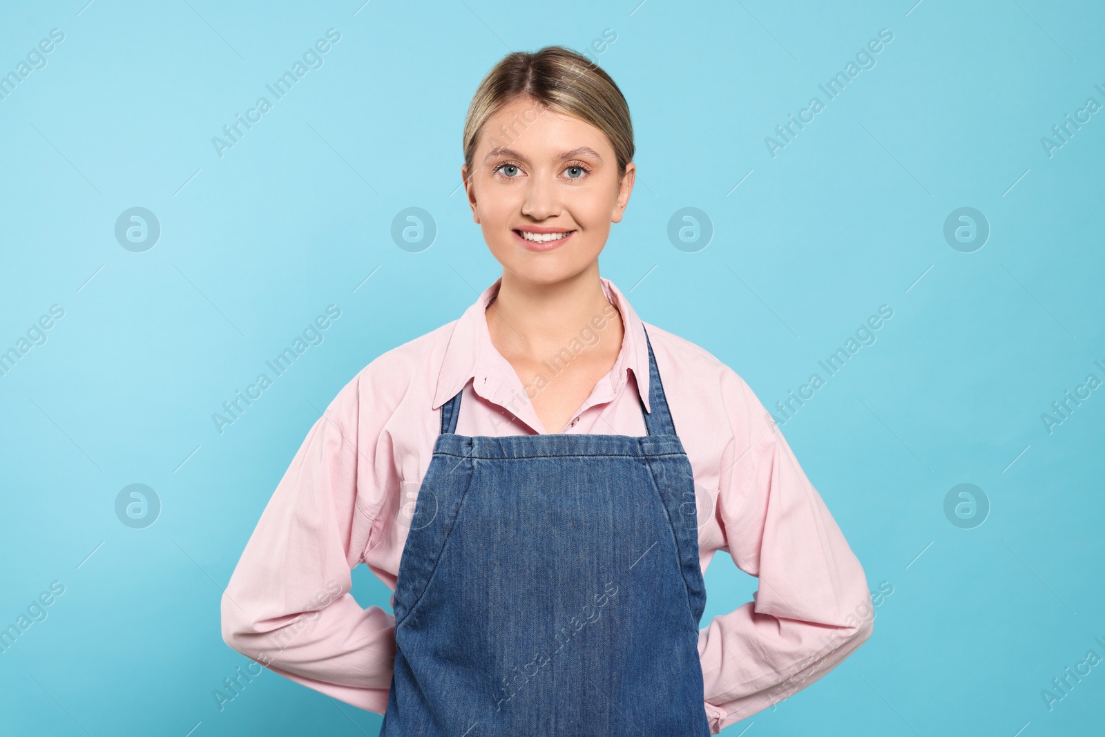 Photo of Beautiful young woman in denim apron on light blue background