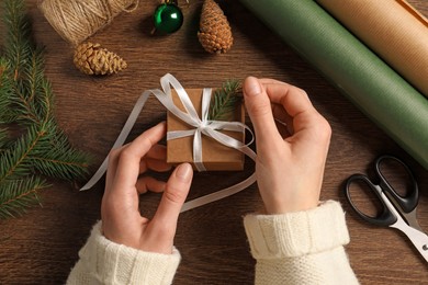 Woman decorating gift box at wooden table, top view. Christmas present