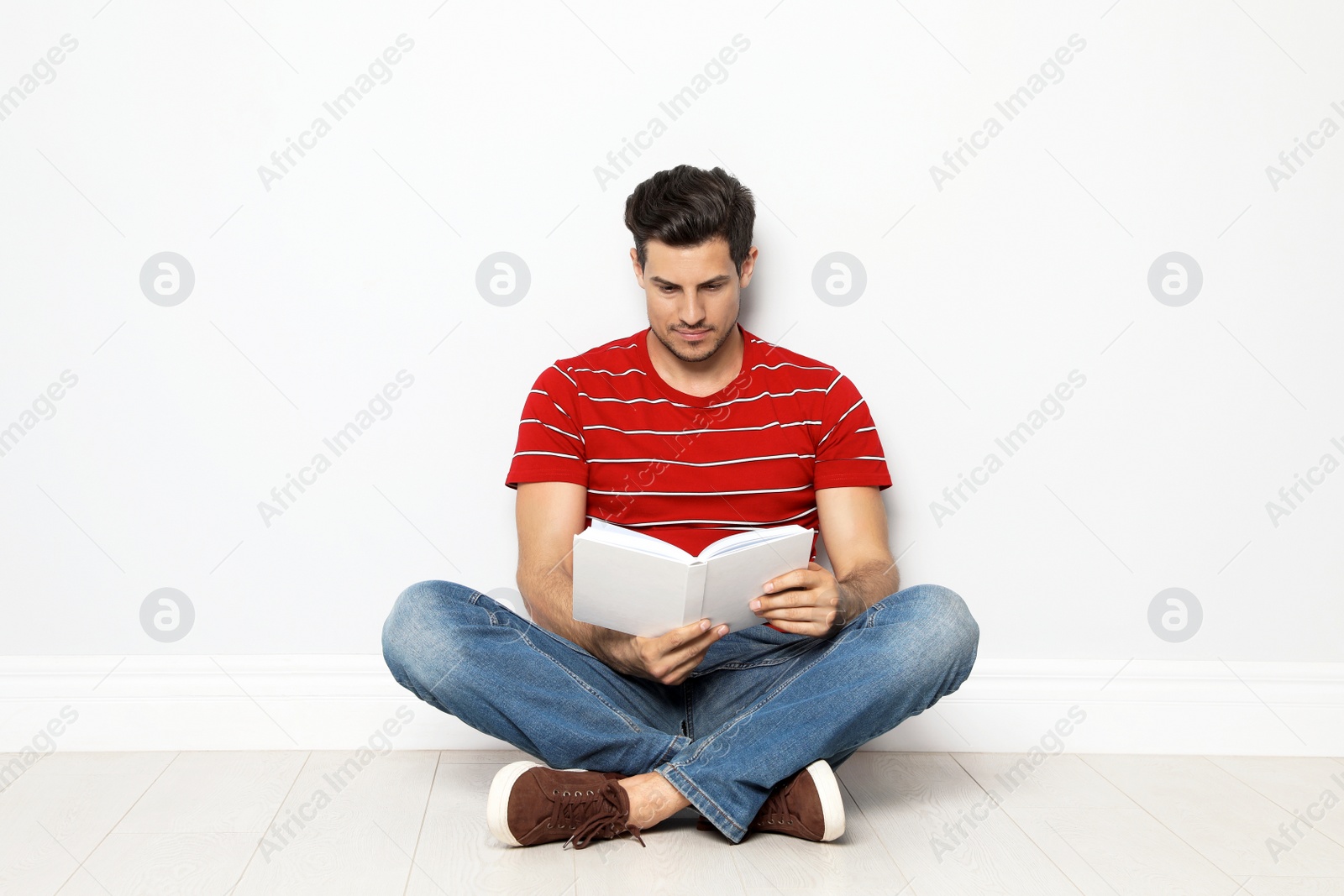 Photo of Handsome man reading book on floor near white wall