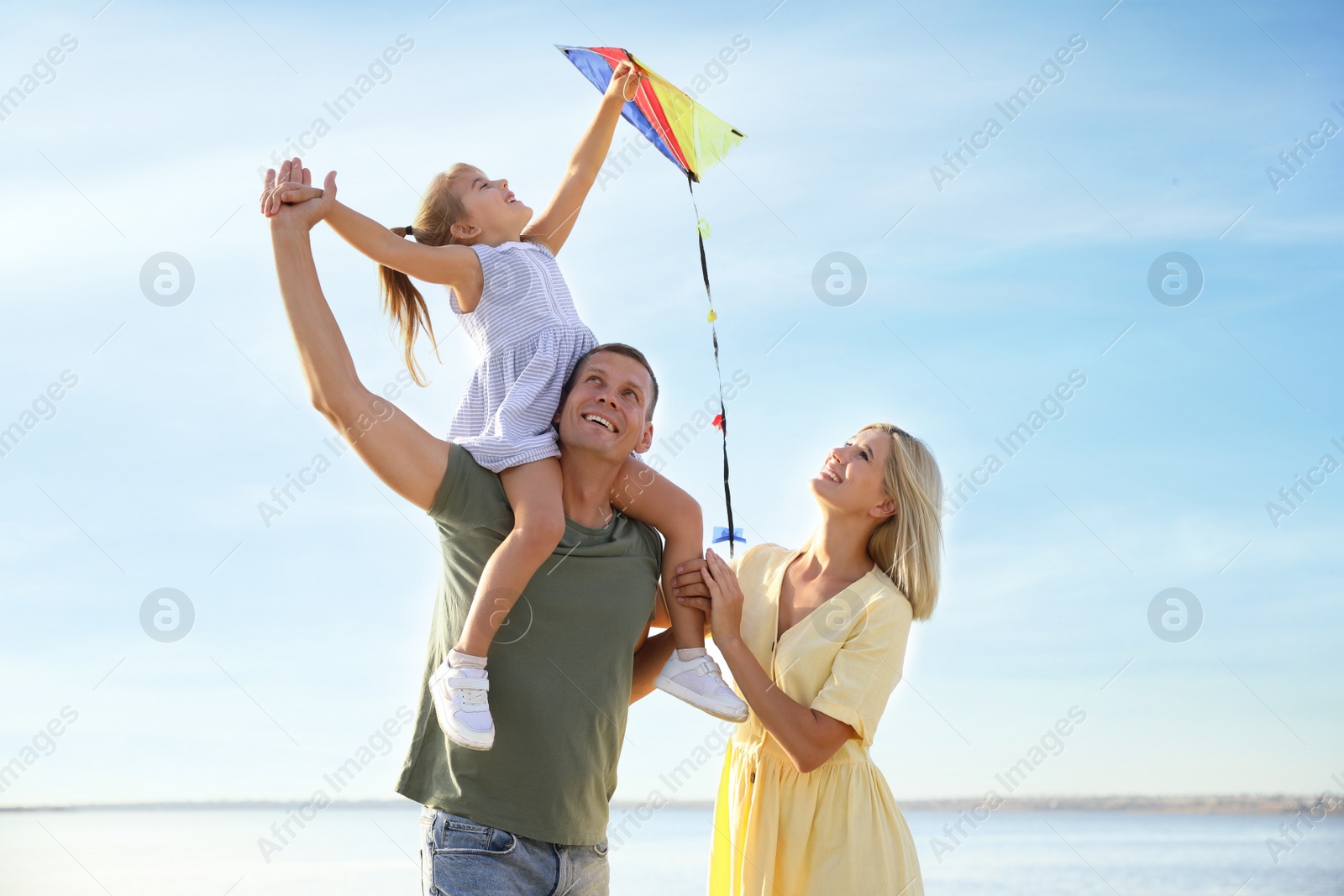 Photo of Happy parents with their child playing with kite on beach. Spending time in nature