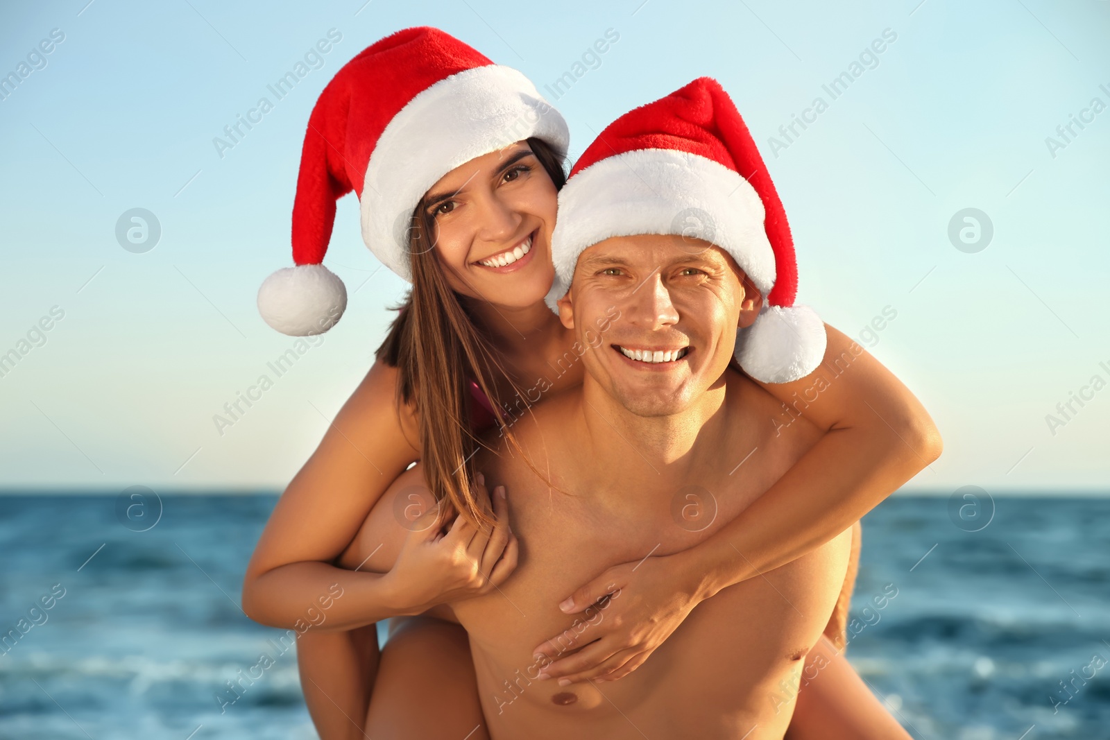 Photo of Happy couple with Santa hats together on beach. Christmas vacation