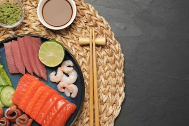 Photo of Tasty salmon slices, shrimp, cucumber and tuna on black table, top view with space for text. Delicious sashimi dish