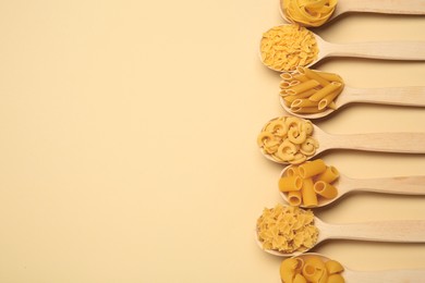 Photo of Different types of pasta in spoons on beige background, flat lay. Space for text