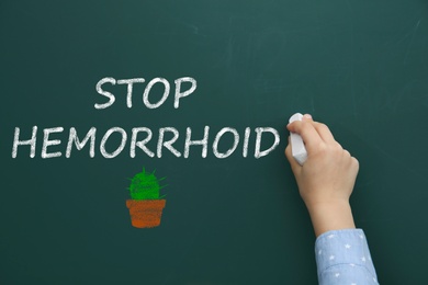 Image of Little child writing phrase Stop Hemorrhoid on chalkboard, closeup
