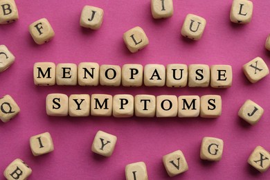 Photo of Wooden cubes with words Menopause Symptoms on pink background, flat lay