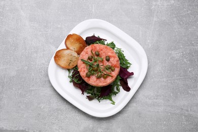 Photo of Tasty salmon tartare with greens and croutons on grey table, top view