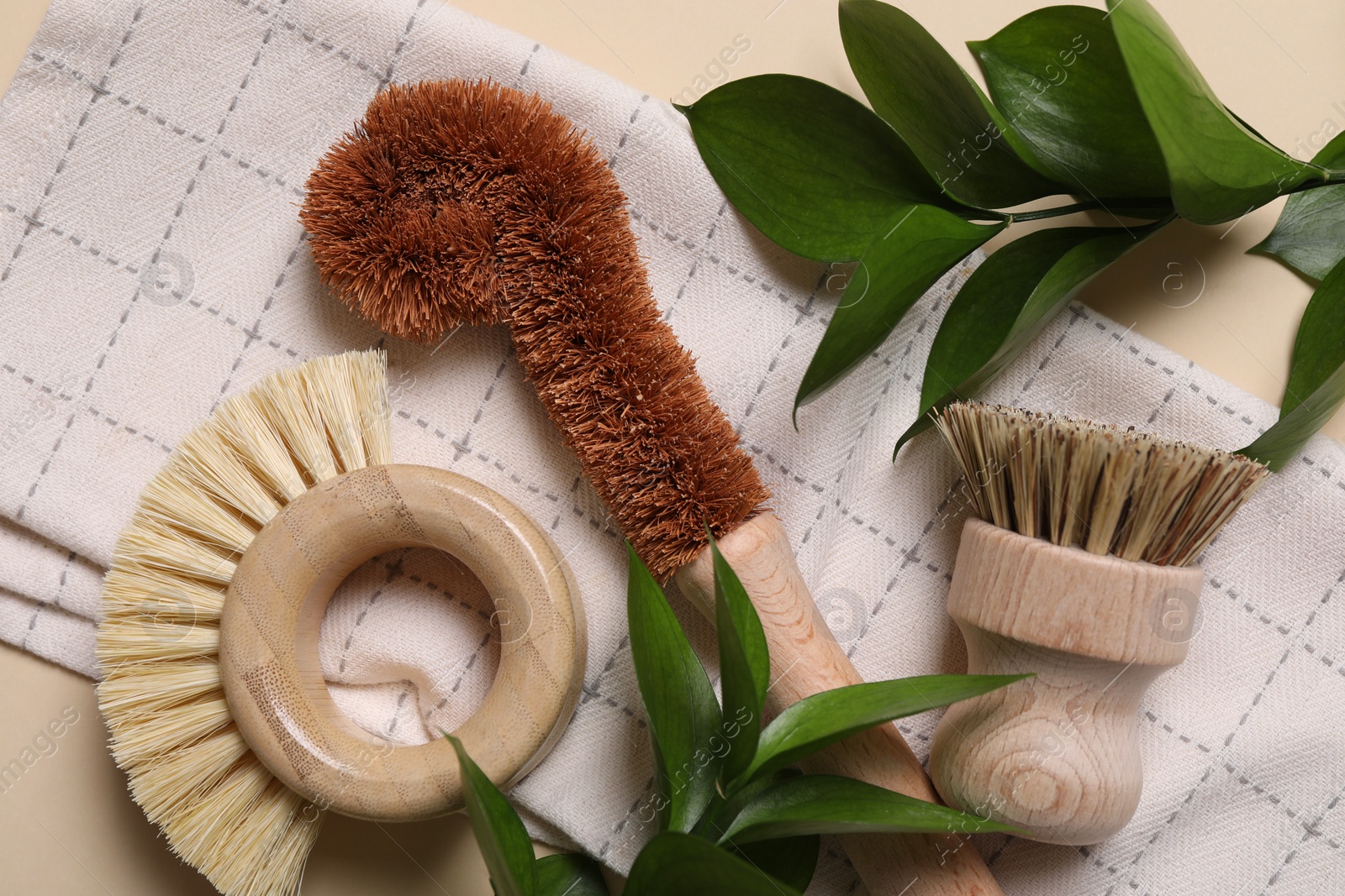 Photo of Cleaning brushes, towel and green leaves on beige background, top view