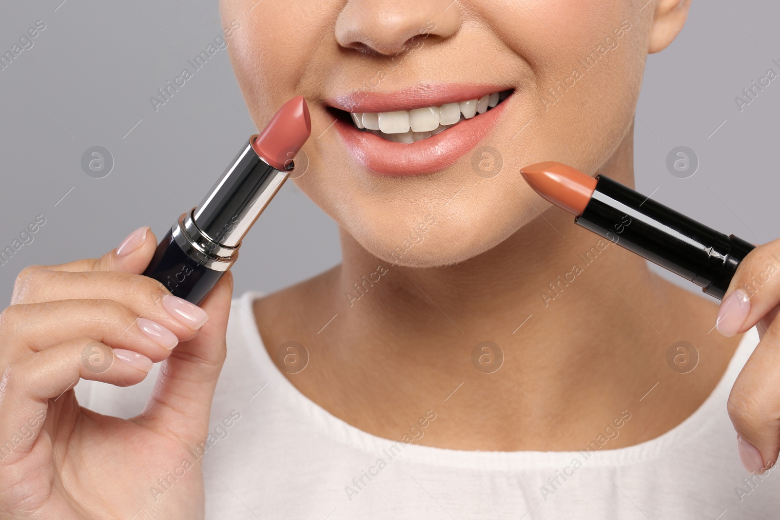 Photo of Young woman with lipsticks on gray background, closeup