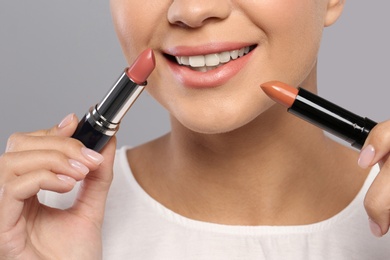 Young woman with lipsticks on gray background, closeup